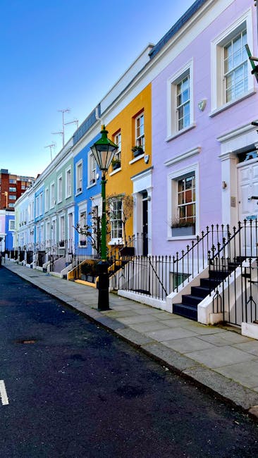 A narrow residential street in Fortune Green and Iverson Road, featuring a cobblestone-edged asphalt road curving gently to the right. The scene includes multi-story brick houses with white-framed sas